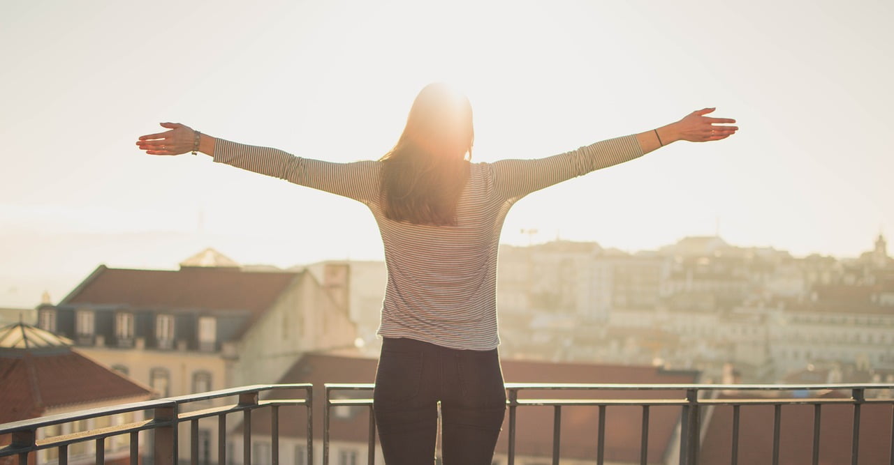 Woman at sunset on a city balcony, arms outstretched