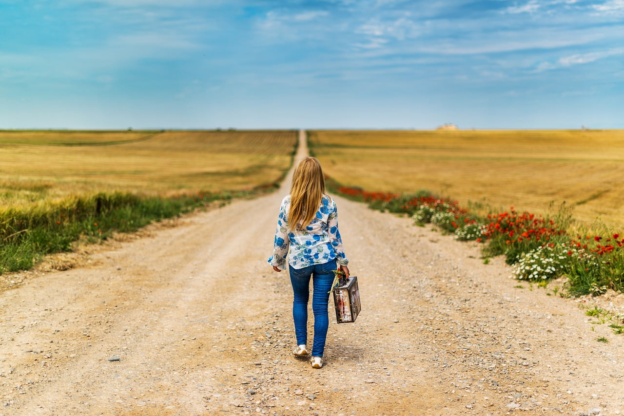 Woman walking down a country road with a suitcase