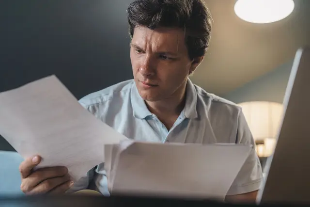 Man frowning as he reviews separation agreement paperwork at his laptop