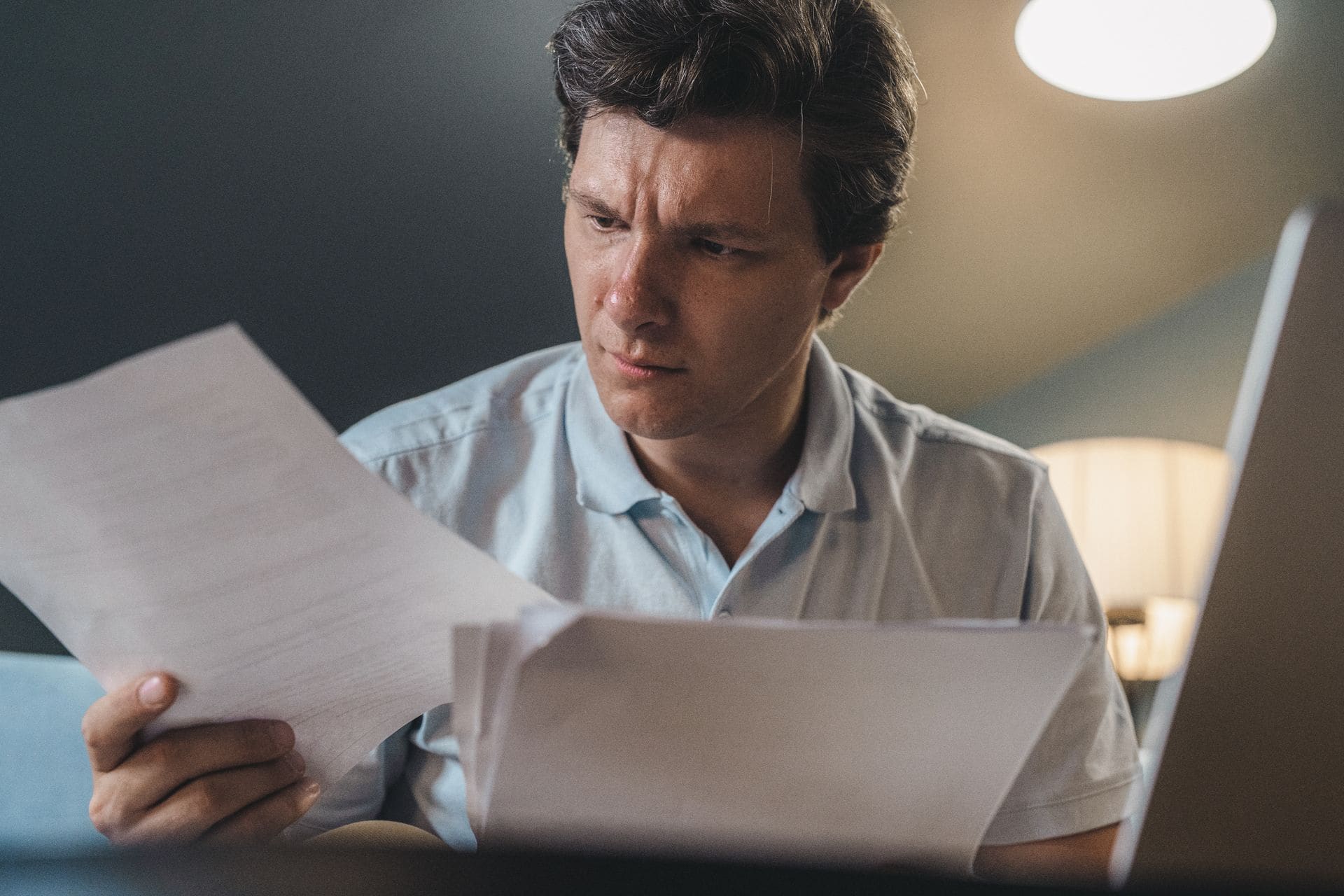 Man frowning as he reviews separation agreement paperwork at his laptop