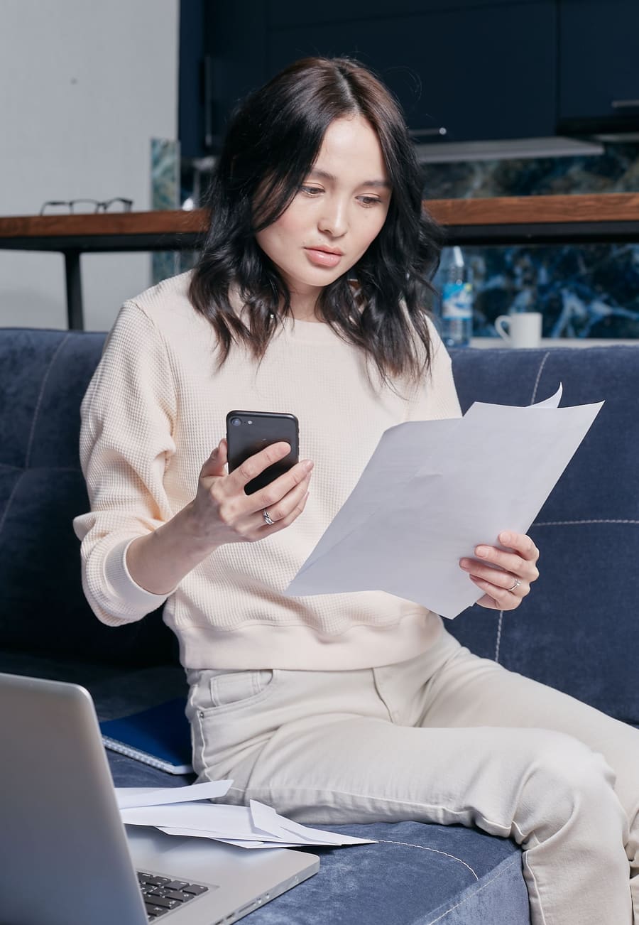 Woman on a couch reviewing separation and divorce documents while looking up a question on her phone